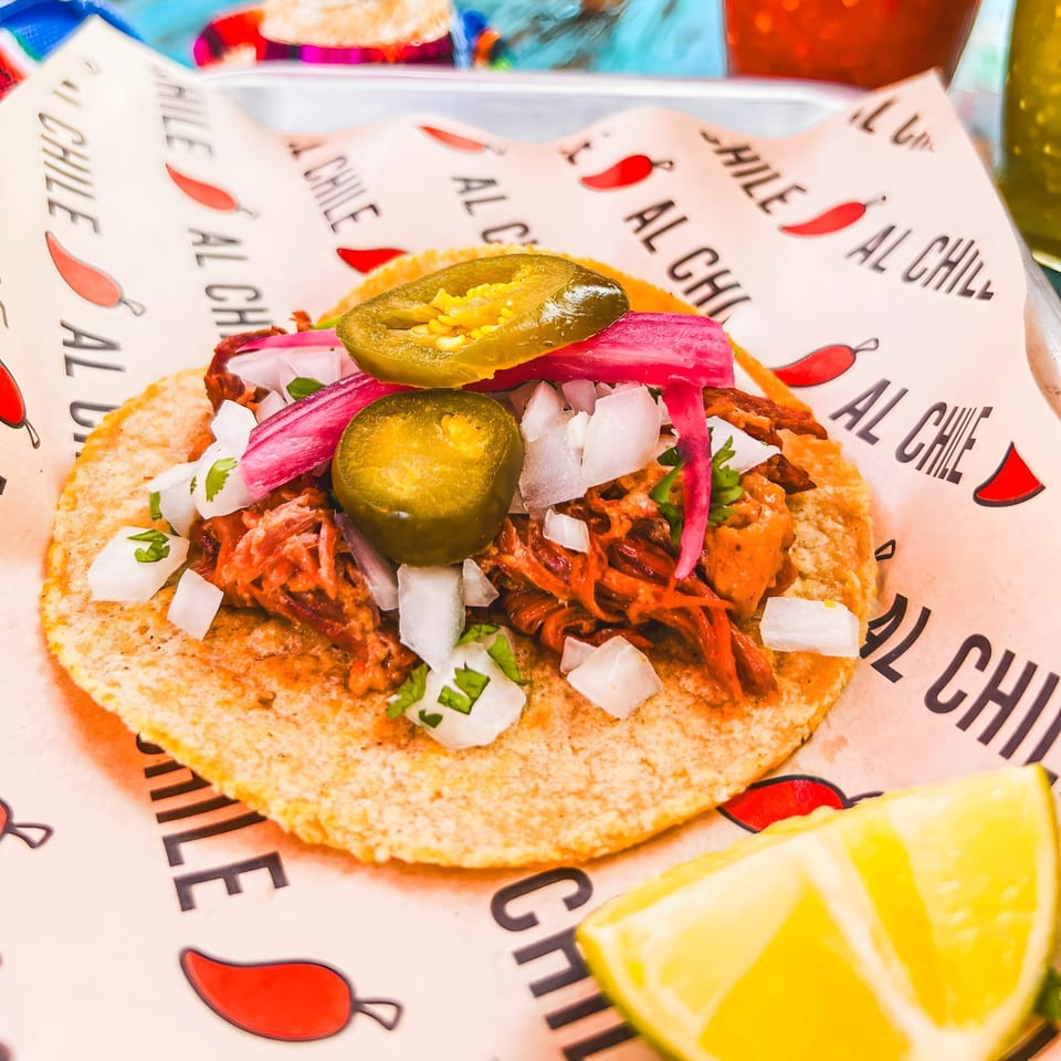 Al Chile Taco Bar's taco with meat, pickled onions, white onions, and jalapeños, with a lime wedge.