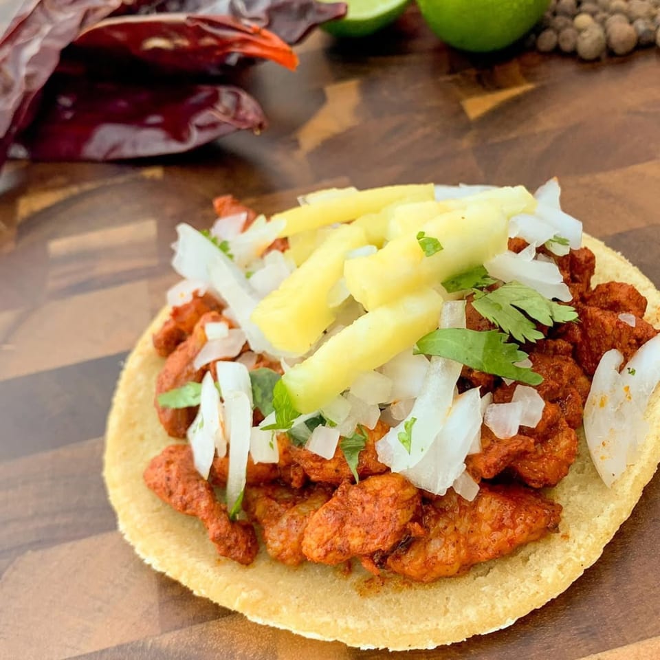 Al Pastor taco with marinated pork, pineapple, onions, and cilantro on a corn tortilla.