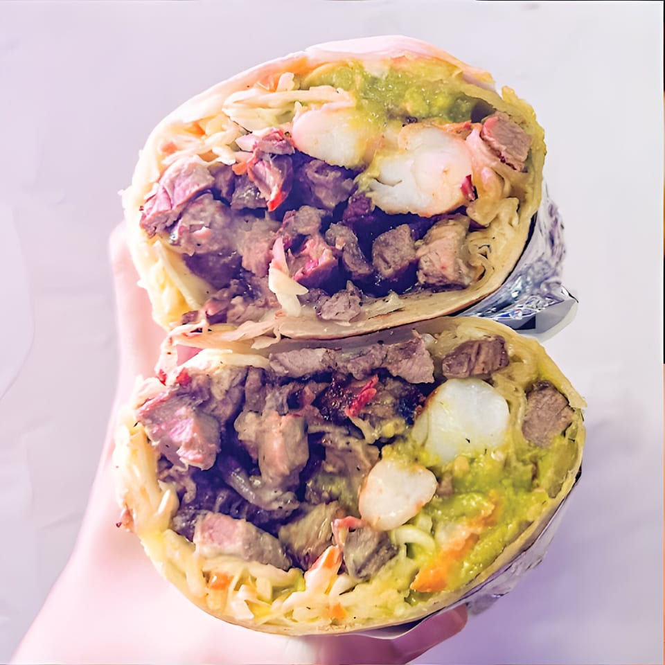 A large Al Chile Taco Bar burrito, cut in half, revealing steak, shrimp, guacamole, and cabbage.