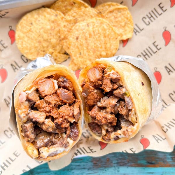 Two halves of a large Al Chile Taco Bar burrito, filled with meat and cheese, with tortilla chips.