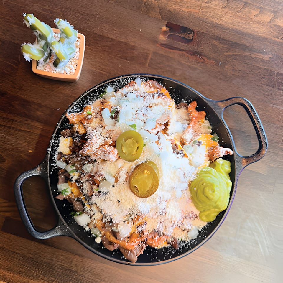 Al Chile Taco Bar's loaded nachos with cheese, jalapeños, and guacamole in a cast iron pan.