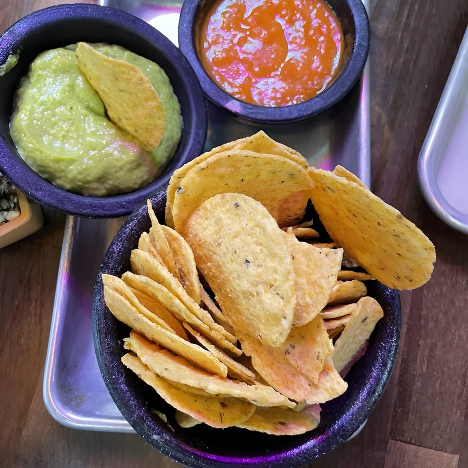 Al Chile Taco Bar's guacamole, salsa, and tortilla chips in dark bowls on a metal tray.